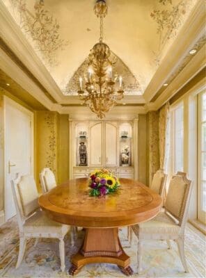 A dining room with a table and chairs, chandelier and windows.